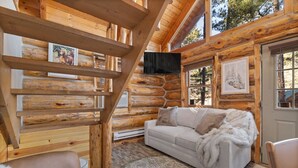 Ein rustikales Blockhaus-Interieur mit einer Couch, einem Kamin und einer Treppe.