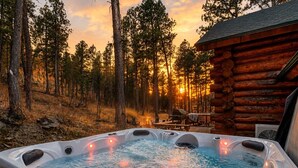 A hot tub in a forested area with a wooden cabin in the background. - Great Lodge at Hillside: Iconic 6K Sqft Log Lodge (Rapid City)