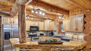 A rustic kitchen with wooden cabinets, a stainless steel refrigerator, a microwave, a stove, and a sink. - Great Lodge at Hillside: Iconic 6K Sqft Log Lodge (Rapid City)