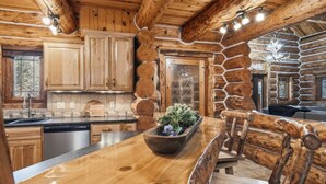 A rustic cabin-style kitchen with wooden cabinets, a stone fireplace, and a wooden dining table with a plant centerpiece. - Great Lodge at Hillside: Iconic 6K Sqft Log Lodge (Rapid City)
