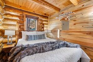 Camera da rifugio in legno con un letto, cuscini, una coperta in pelliccia sintetica, un quadro e un attaccapanni a sospensione.