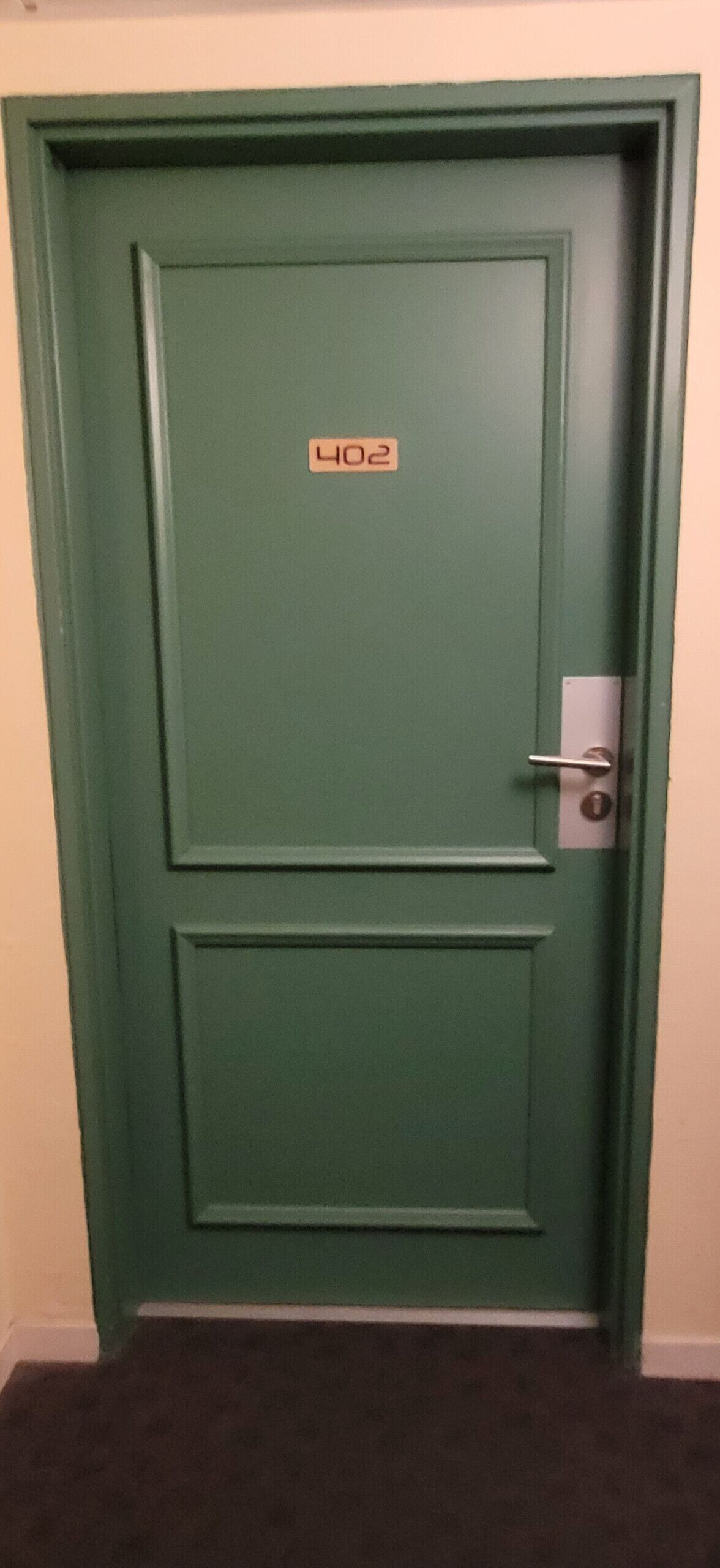 Una porta verde con una targa che riporta il numero '402' e una maniglia.