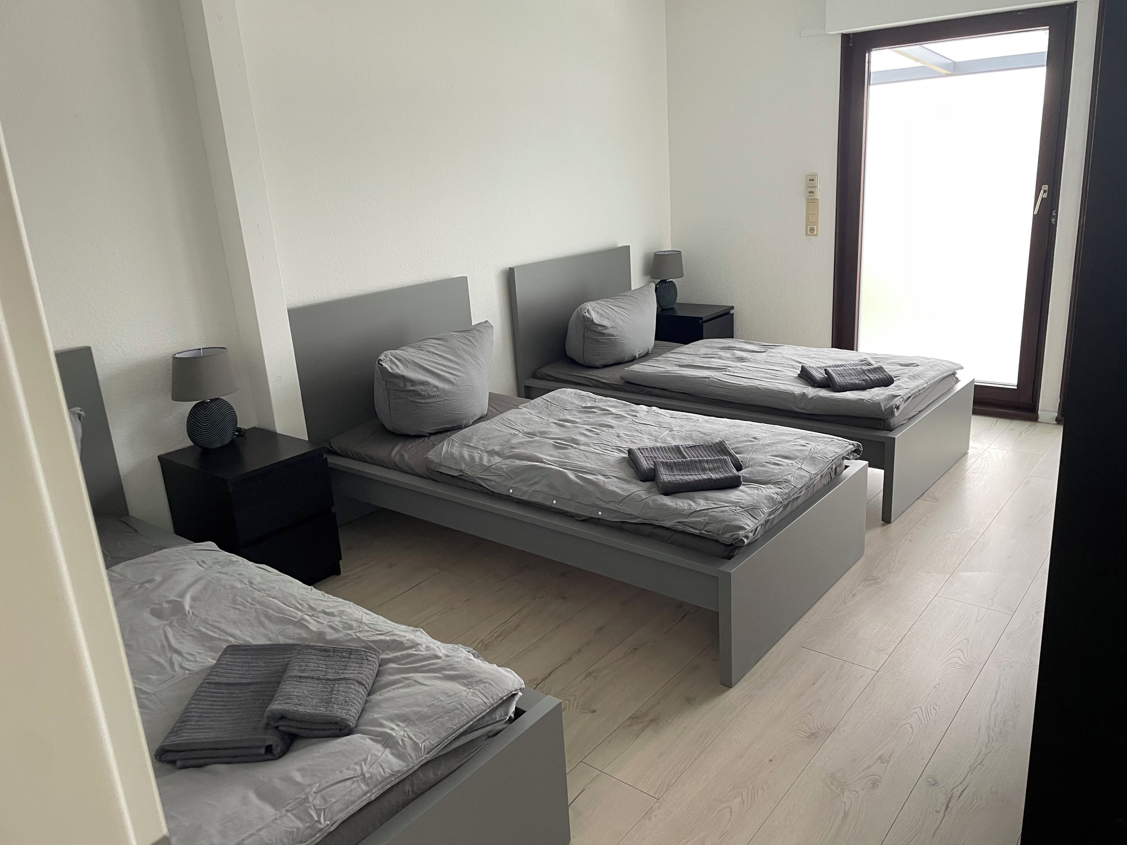 Una habitación de hotel con tres camas individuales, una mesita y una mesita de noche con una lámpara.