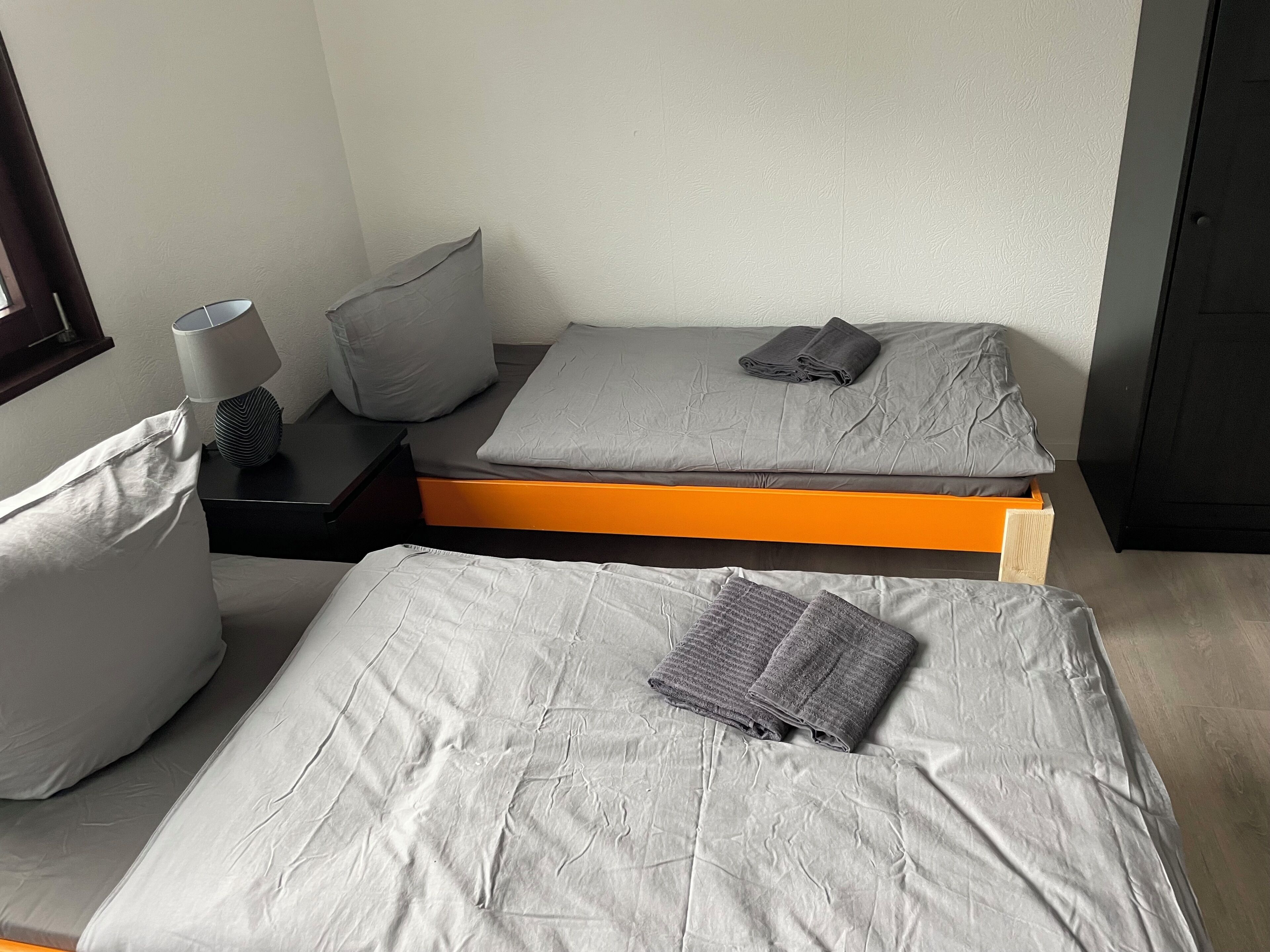 A room with two beds, a nightstand, a lamp, and a window.