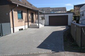 A residential driveway leading to a garage, a brick house with a window, and a clear sky. - Blauer Stein - Pure - bl07-haus (Pulheim)