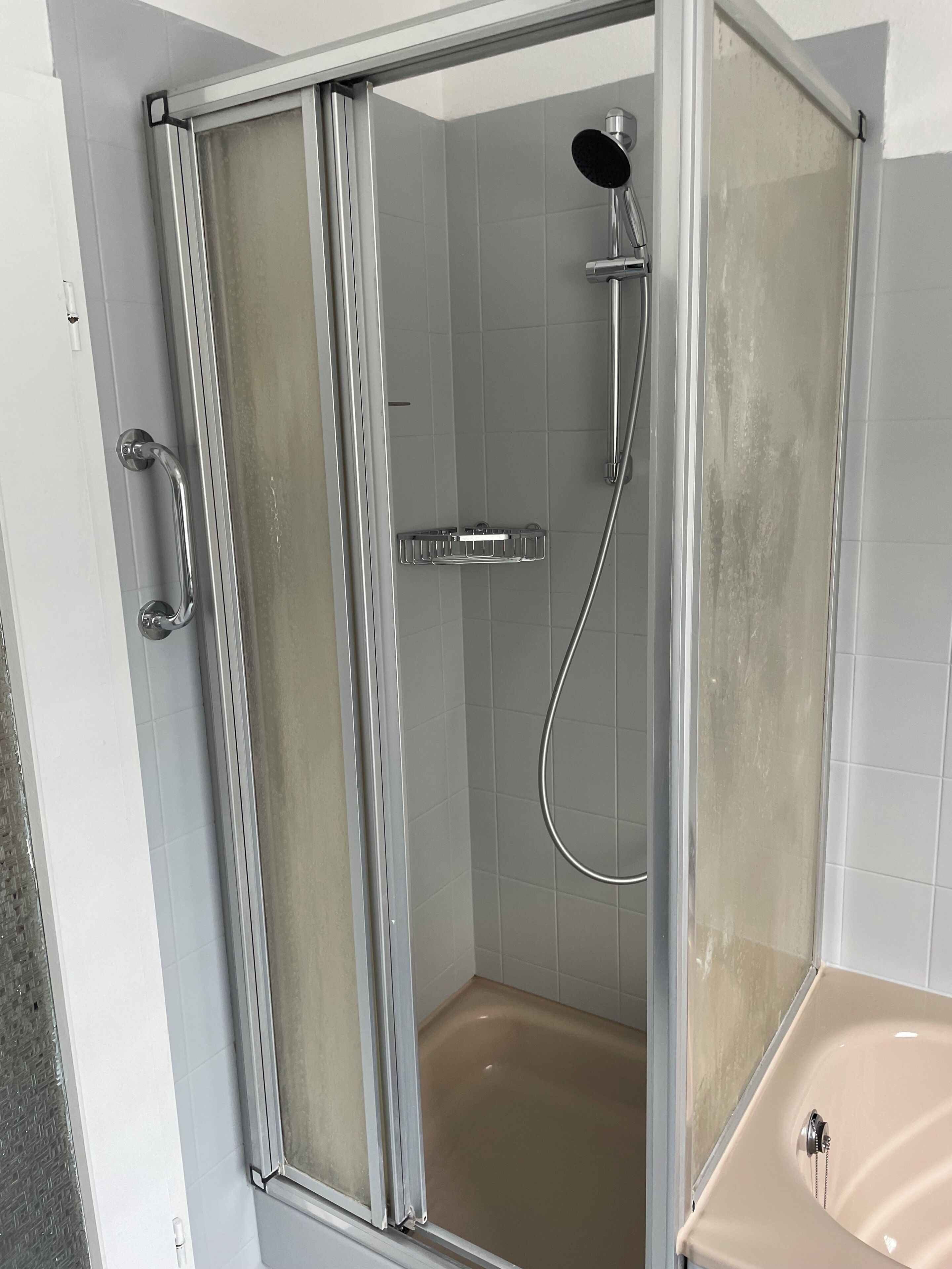 A shower enclosure with a glass door, a handheld showerhead, and a handheld shower attachment.
