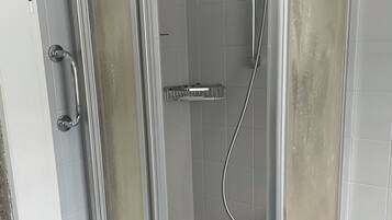 A shower enclosure with a glass door, a handheld showerhead, and a handheld shower attachment.