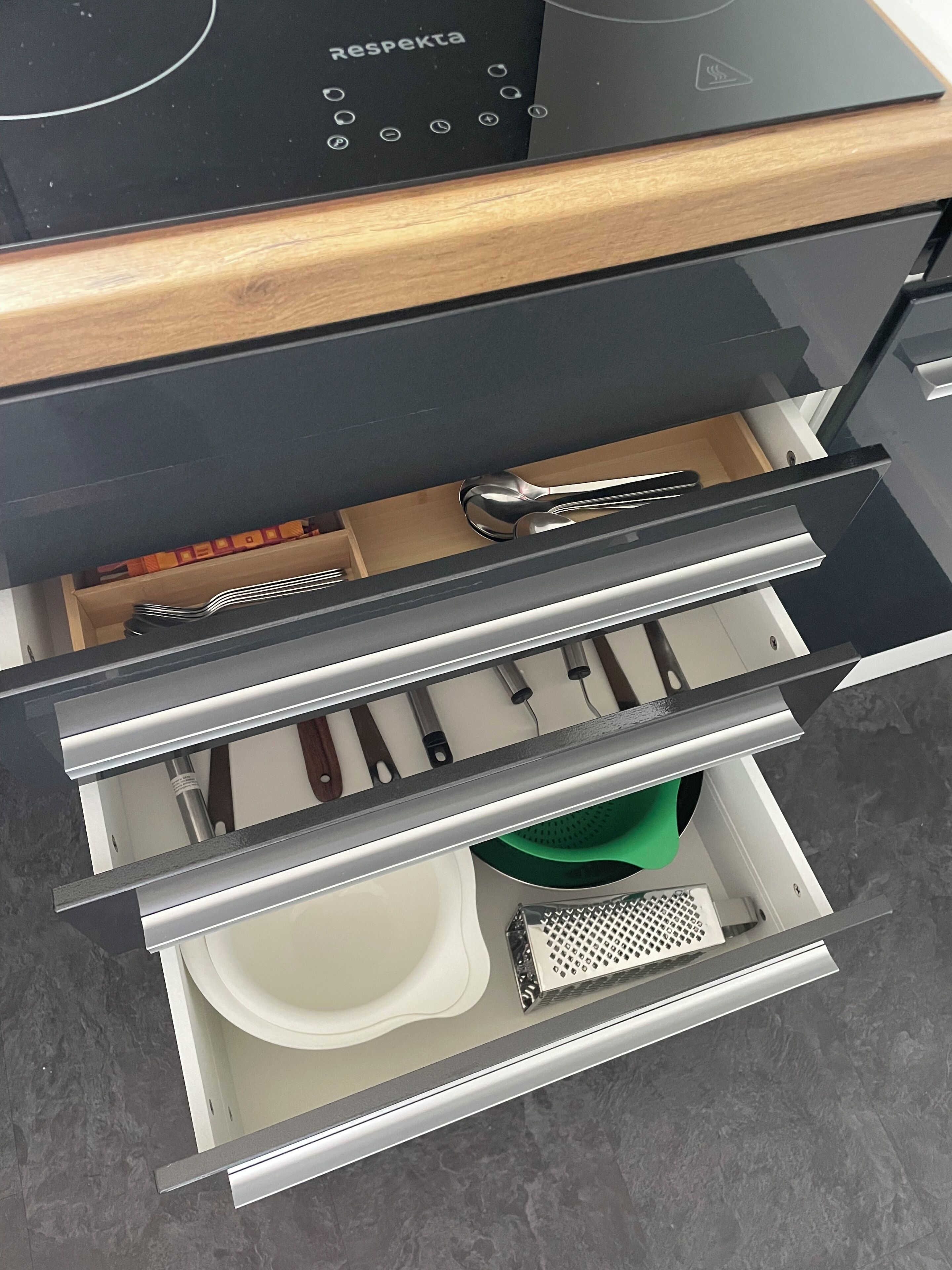 Un cajón de cocina con utensilios, un colador y un rallador.