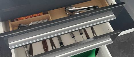 Un cajón de cocina con utensilios, un colador y un rallador.