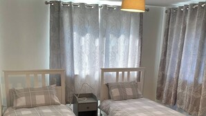 Un dormitorio con dos camas individuales, una mesita de noche, una lámpara y cortinas.