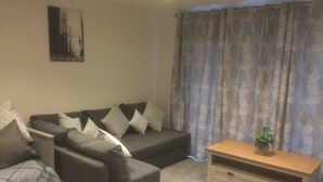 Una sala de estar con un sofá gris, una mesita de madera y una cortina estampada.
