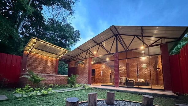 A modern outdoor patio area with a fire pit, wooden seating, and a covered seating area with glass doors. - Country House in Tingo Maria - Adelaide Resort (Tingo María)