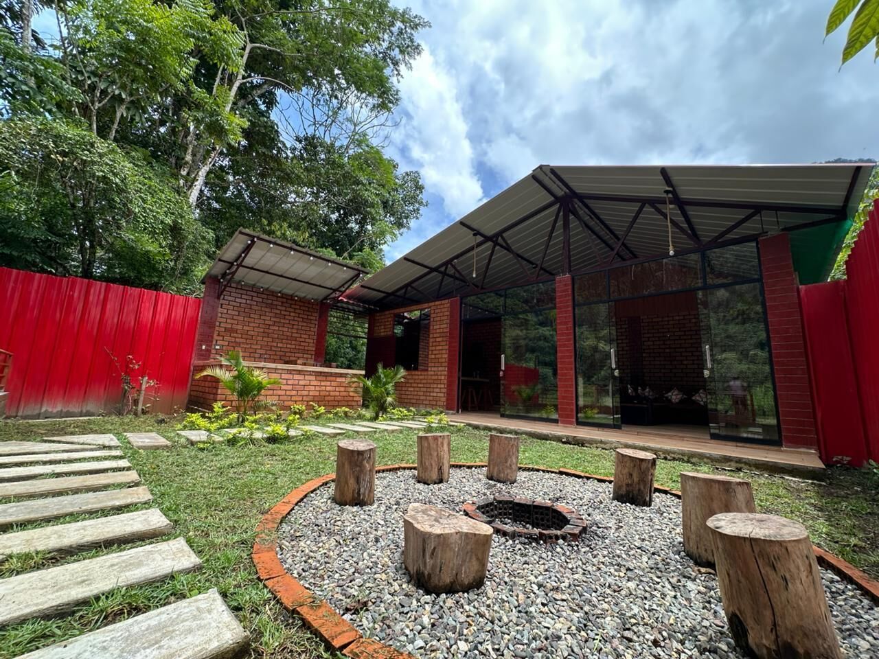 Un espace extérieur moderne aménagé avec des sièges, doté d’un foyer, et entouré d’un cercle de gravier et de tabourets en bois.