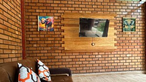 A room with a brick wall, a mounted TV, and a sofa with patterned cushions. - Country House in Tingo Maria - Adelaide Resort (Tingo María)