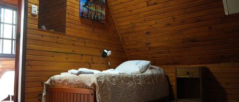 Quarto de cabana de madeira com uma cama, um criado-mudo, uma luminária na parede e um quadro.