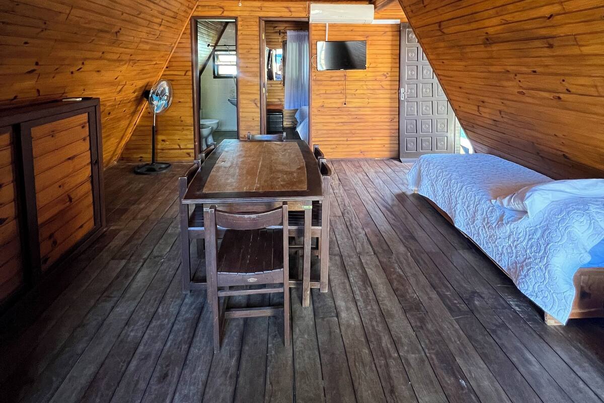 Un intérieur en bois comprenant une table et des chaises, un lit et un téléviseur fixé au mur.