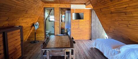 A wooden interior with a dining table and chairs, a bed, and a TV mounted on the wall.
