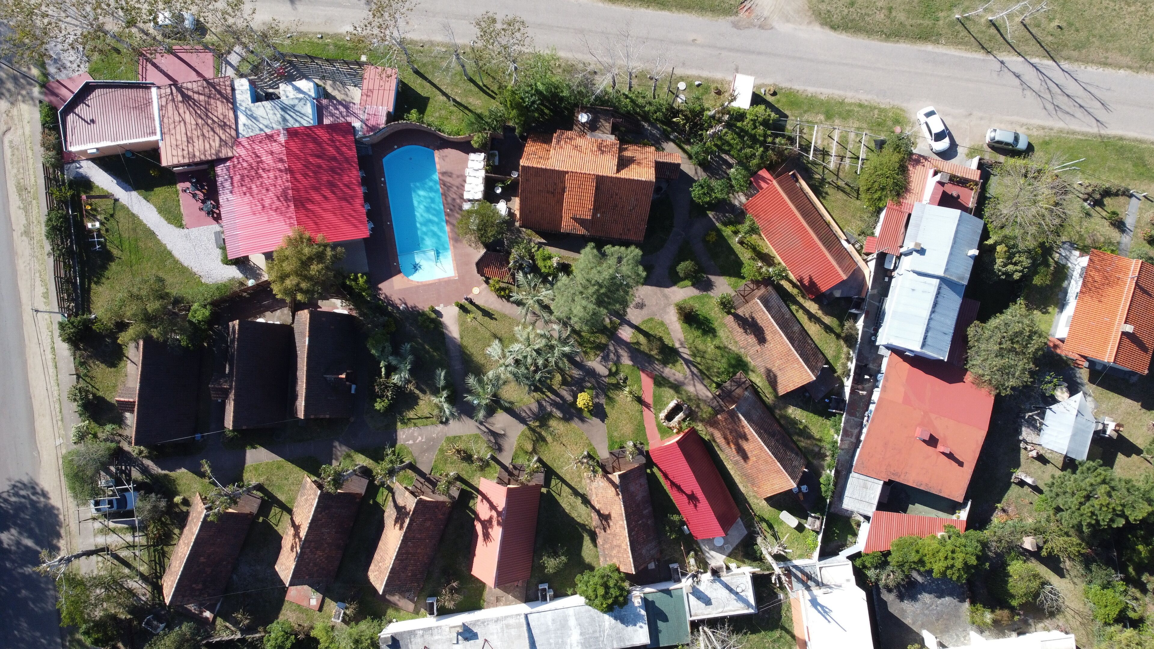 An aerial view of a residential area with multiple houses, a swimming pool, and a road.