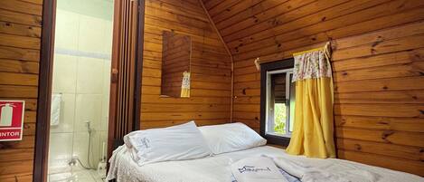Una habitación de cabaña de madera con cama, una mesita y una zona de ducha.
