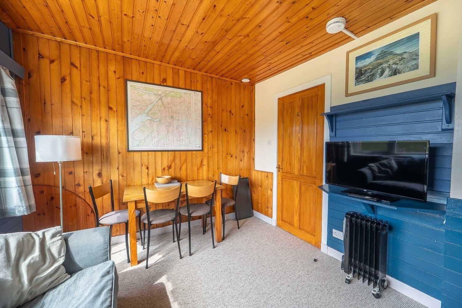 Une pièce chaleureuse aux murs en bois, avec une table à manger et des chaises, un téléviseur et un radiateur.