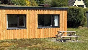 Een houten hut met twee grote ramen en een picknicktafel ervoor.