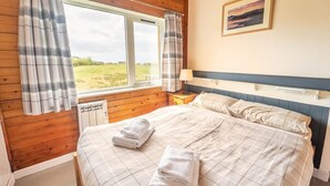 Een slaapkamer met een bed, een nachtkastje, een raam met gordijnen en een schilderij aan de muur.