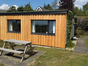 Une cabane en bois avec deux fenêtres, une table de pique-nique et un sentier menant à une maison.