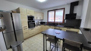 Eine moderne Küche mit Holzausstattung, einem Edelstahlkühlschrank, einer Mikrowelle und einem Herd. Ein Fenster bietet Blick auf umliegende Gebäude.