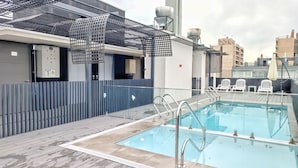 Une piscine sur le toit, entourée d’une barrière de sécurité en métal, avec une chaise et une fontaine d’eau à proximité.