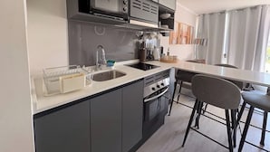 Une cuisine moderne avec des meubles de couleur sombre, un évier en acier inoxydable et une cuisinière à gaz. On y trouve également un coin repas avec une table et des chaises.