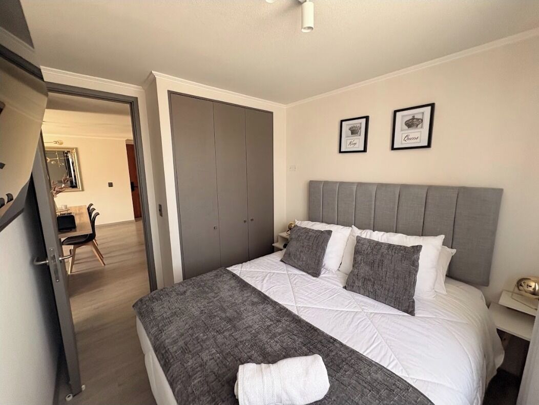 Une chambre à coucher bien rangée, avec un grand lit, une tête de lit grise et deux tableaux encadrés accrochés au mur.