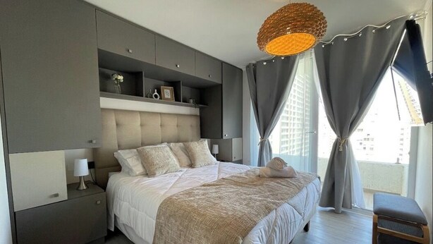 Une chambre moderne avec un grand lit, des étagères intégrées, une table de chevet et un luminaire suspendu.