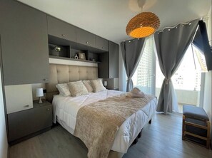 Een moderne slaapkamer met een groot bed, inbouwkasten, een nachtkastje en een hanglamp.