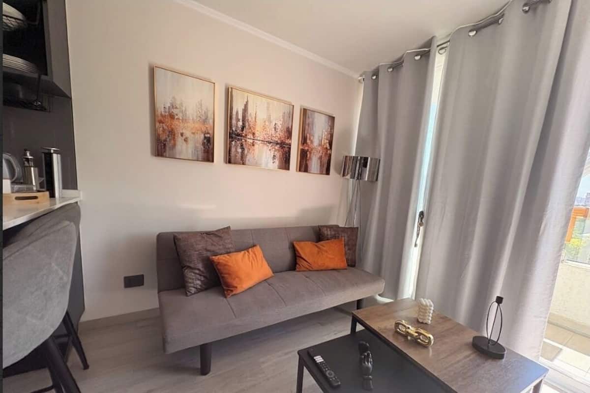 Un saló modern amb un sofà gris, dos coixins taronja, una taula de centre i obra d'art a la paret.