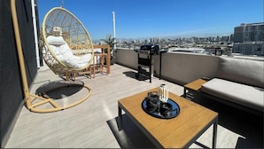 Une terrasse sur le toit avec un fauteuil suspendu, un canapé, une table et un barbecue.