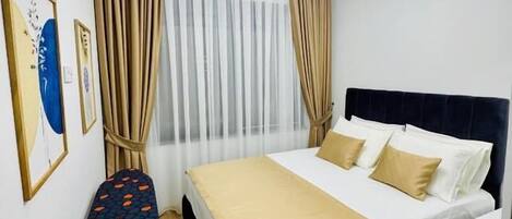 A hotel room with a bed, curtains, a ceiling fan, and an ironing board.
