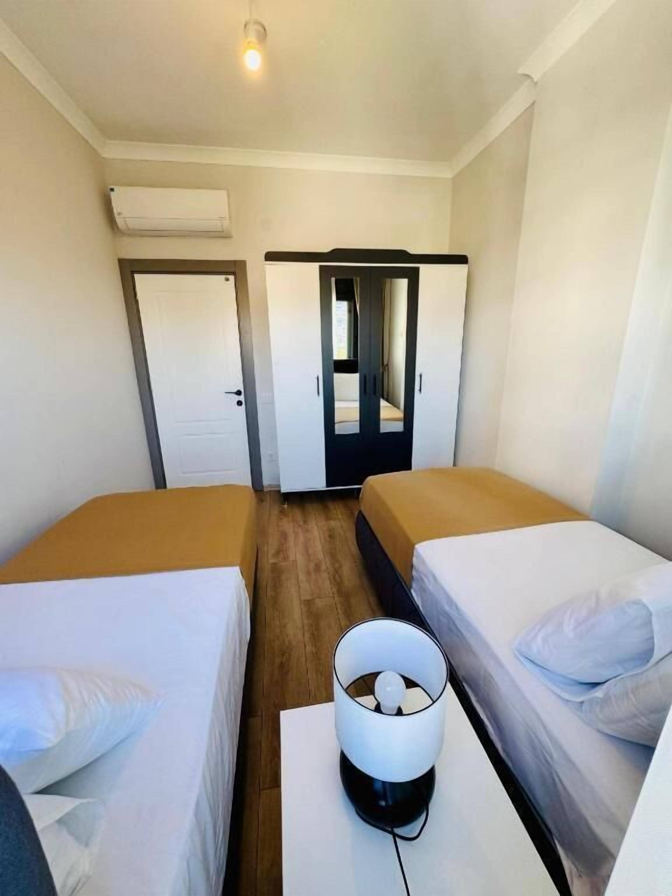 A hotel room with two single beds, a small table with a lamp, and a door leading to a bathroom.