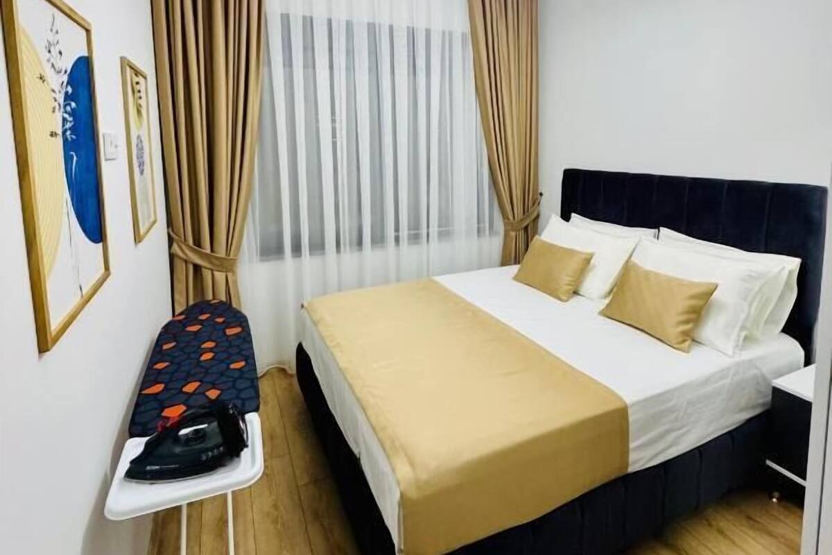 Une chambre d’hôtel avec un lit, des rideaux, un luminaire au plafond et une planche à repasser.