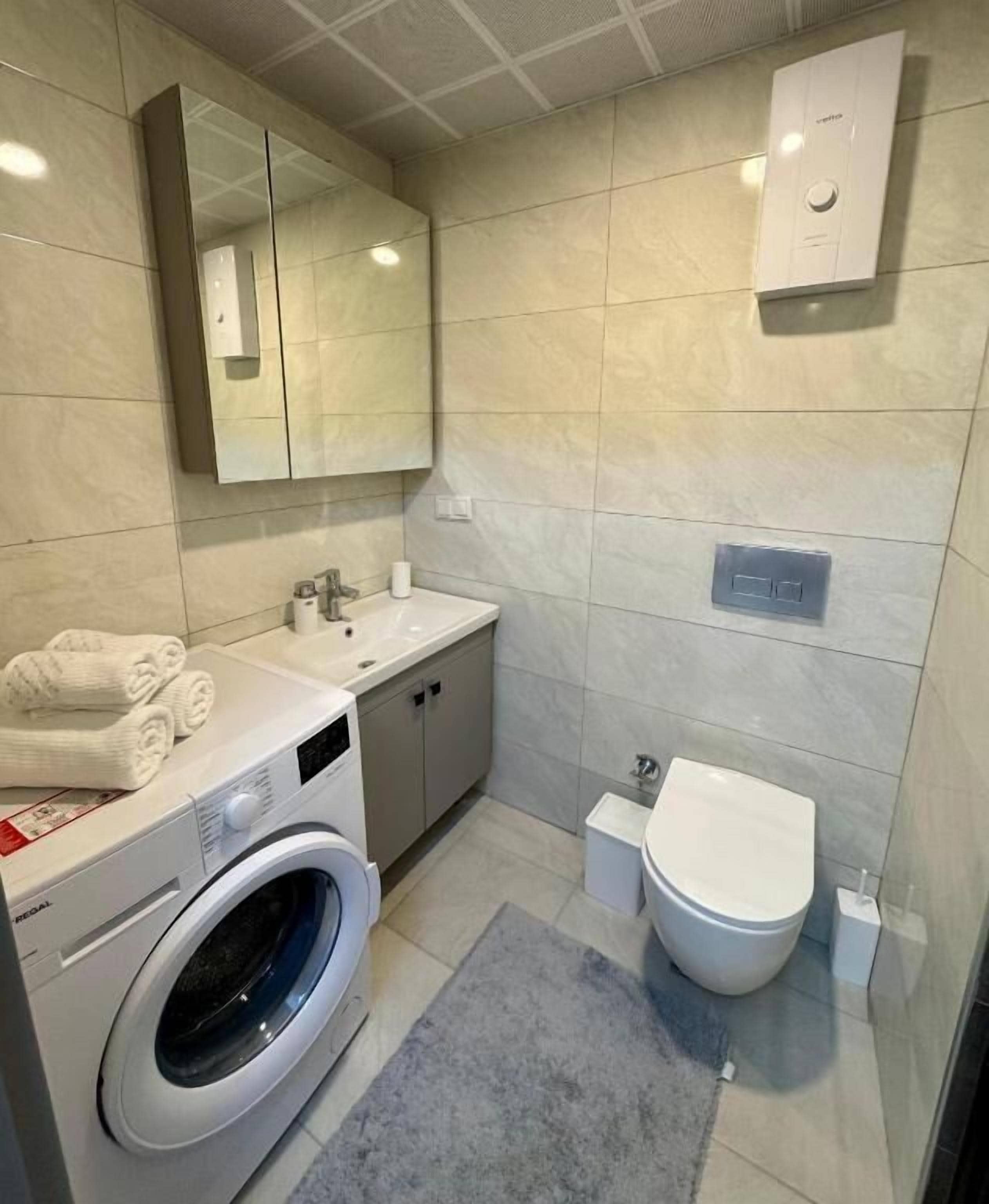 A modern bathroom with a washing machine, sink, toilet, and a large mirror.