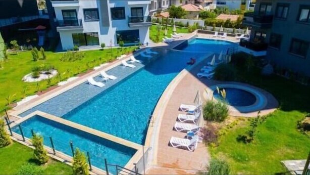 Una amplia piscina con varias secciones, rodeada de tumbonas y un jardín ajardinado.