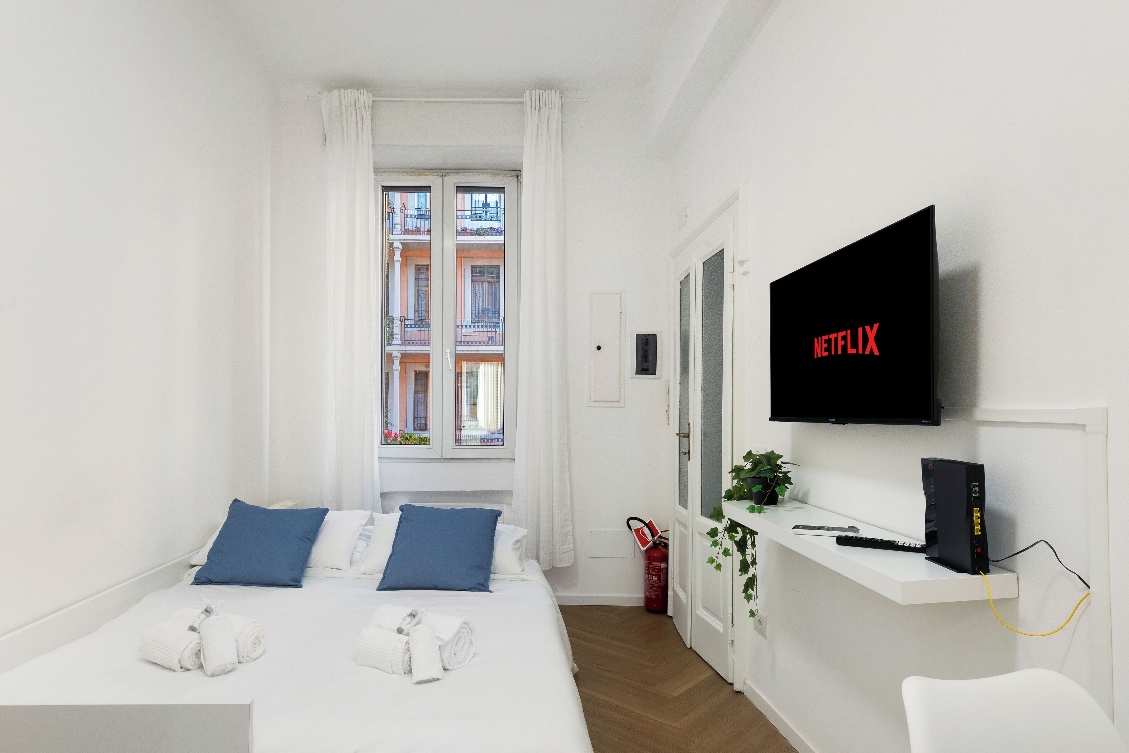Habitación de hotel moderna con una cama, un televisor y un escritorio pequeño con una planta.