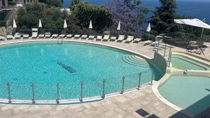 Uma piscina ampla e convidativa, com espreguiçadeiras e guarda-sóis, cercada por um deck de pedra e com vista panorâmica.