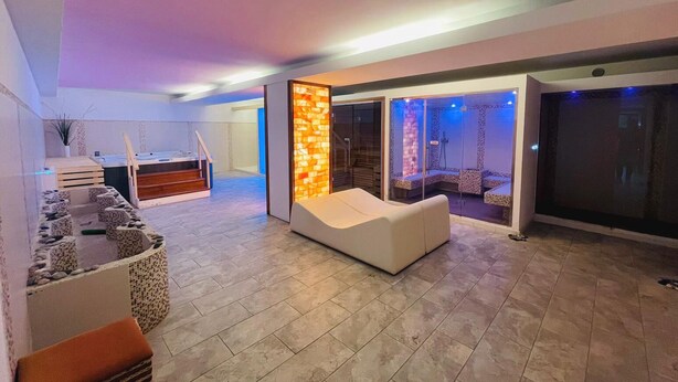 A modern living area with a sofa, a small seating area with cushions, a staircase, and a glass partition with a stone wall. - Residence Letojanni (Letojanni)
