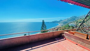 Uma varanda com vista para o mar e paisagem montanhosa.