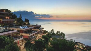 A coastal hotel with multiple balconies overlooking the sea, featuring modern architecture and a serene sunset view. - Residence Letojanni (Letojanni)
