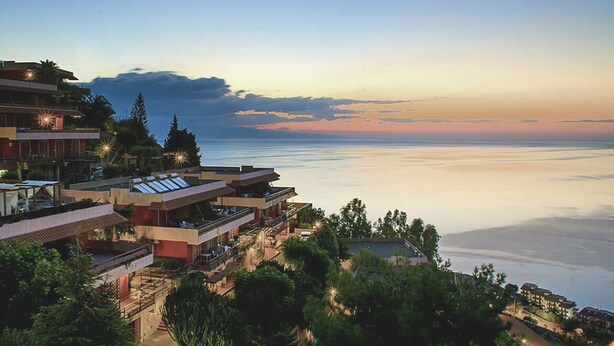 Hotel à beira-mar com várias varandas com vista para o oceano, com arquitetura moderna e uma paisagem serena ao pôr do sol.