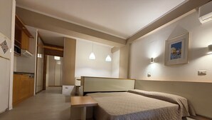 Quarto com cama, mesa de cabeceira e vista para a cozinha e o banheiro.
