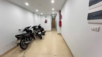 Passadís amb dues motocicletes aparcades a l'esquerra, un detector de fum a la paret i una porta al final.
