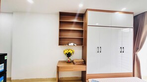 Een slaapkamer met een bed, een houten bureau met een bloevas, een kledingkast en een plankje met een telefoon en headphones.