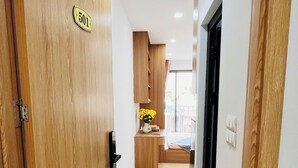 A hallway with a wooden door labeled "501", a small wooden table with a vase of yellow flowers, and a view of a balcony with a railing.